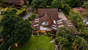 A large house with a tiled roof, surrounded by lush greenery and a well-maintained lawn. - HOTEL CASA MADERO (Envigado)