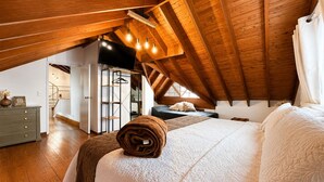 A bedroom with a sloped ceiling, a bed with white bedding, a wooden dresser, and a hanging light fixture. - HOTEL CASA MADERO (Envigado)