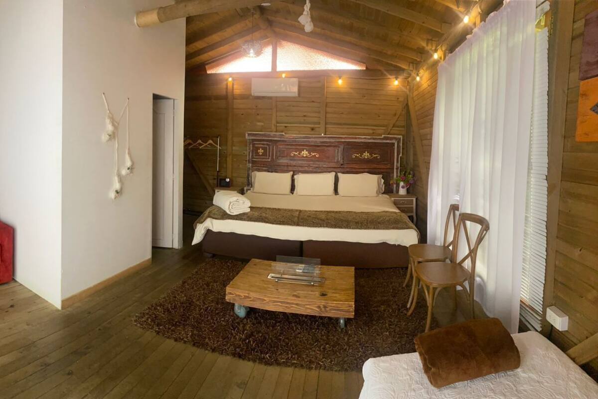 A cozy room with a wooden ceiling, a red sofa, a bed with a wooden headboard, a small wooden table, and a chair.
