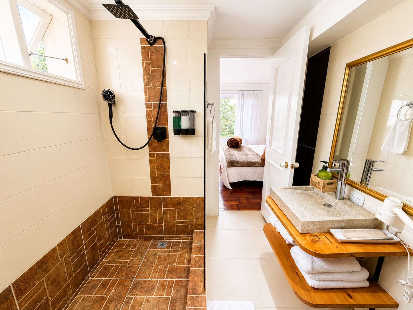 A bathroom with a shower, a sink, a mirror, and a bed in the adjacent room.