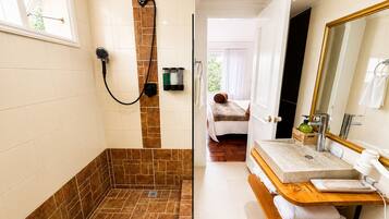 Une salle de bain avec une douche, un lavabo, un miroir et un lit dans la pièce adjacente.