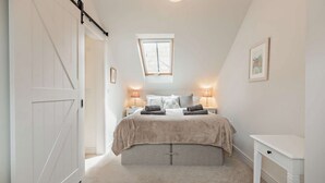 Un dormitorio con una cama grande, dos mesitas de noche con lámparas, una ventana y un armario blanco.
