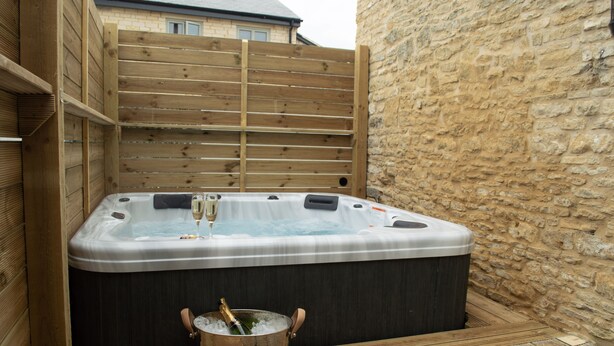 Un jacuzzi con valla de madera y pared de piedra al fondo.