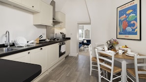 Een moderne keuken met witte kasten, een zwart aanrecht en een eethoek met een houten tafel en witte stoelen.