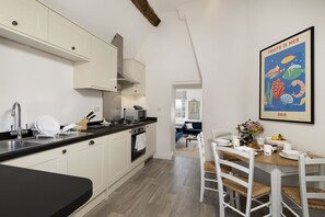 Une cuisine moderne avec des meubles blancs, un plan de travail noir et un coin repas comprenant une table en bois et des chaises blanches.