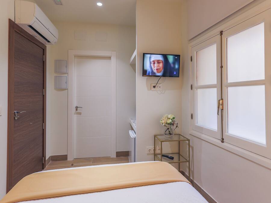 Una habitación de hotel con una cama, un televisor montado en la pared, una puerta de madera y un ventanal con cristal esmerilado.