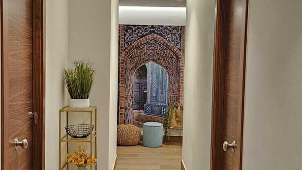 A hallway with wooden flooring, two wooden doors, a plant on a shelf, and a patterned wall in the background. - Dorinda Rooms  (Alicante)