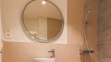 A bathroom with a round mirror, a sink, and a shower.