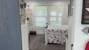Un pasillo estrecho que conduce a un dormitorio con cama, cómoda y ventana con persianas.