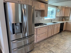 A modern kitchen with stainless steel appliances, wooden cabinets, a built-in oven, and a window with a view. - Silverstrand Beach home (Oxnard)