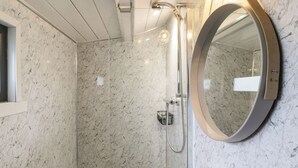 Un baño con ducha de vidrio, un lavabo blanco y un espejo redondo.