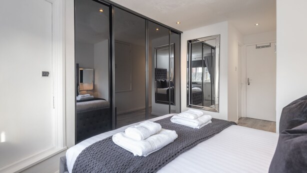 Una habitación de hotel moderna con una cama grande, un armario con puerta corredera y un espejo que refleja la habitación.