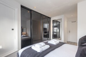 A modern hotel room with a large bed, a sliding door closet, and a mirror reflecting the room. - 2 Bed Town House With Garden in Hackney, London (London)