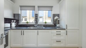 Una cocina moderna con armarios blancos, encimera negra, pileta doble y ventana con persianas.