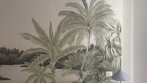 A bedroom with a mural of tropical foliage, a bed with white bedding, and a lamp on a side table. - chiesa russa (Bari)