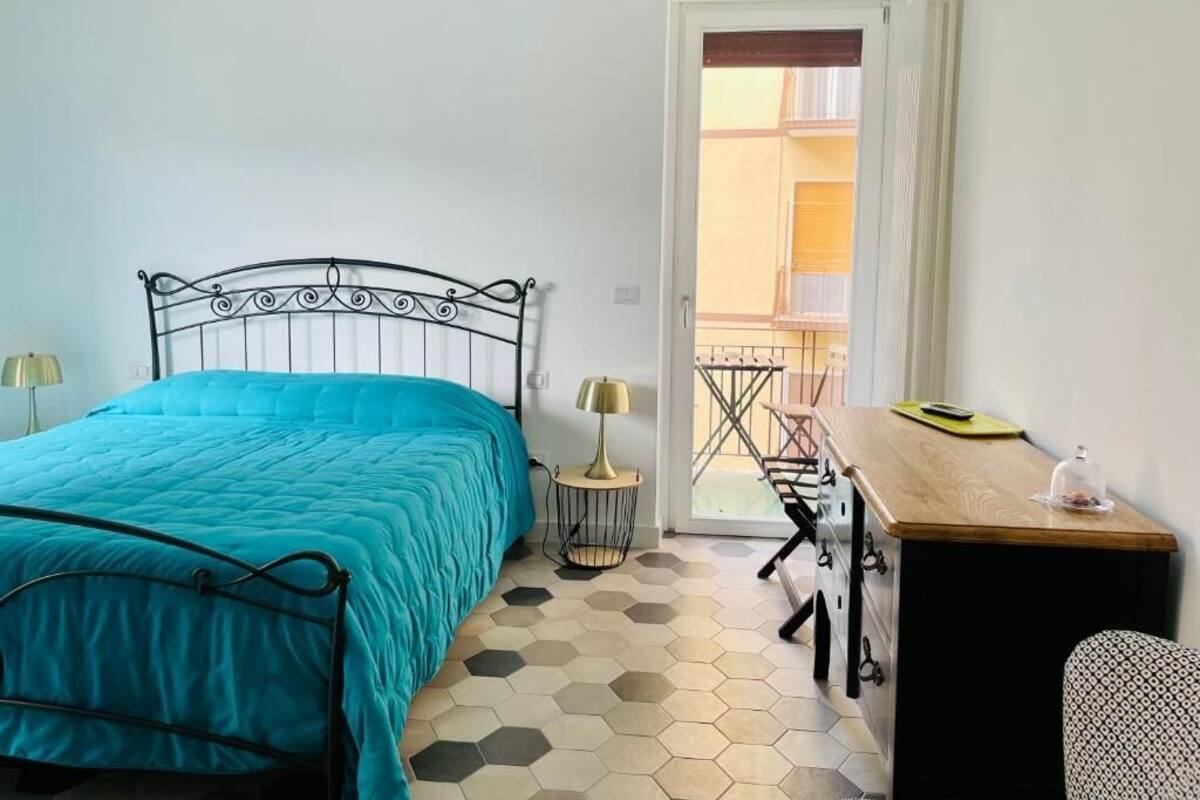 Un dormitorio con cama, escritorio, silla y vistas a un balcón exterior.