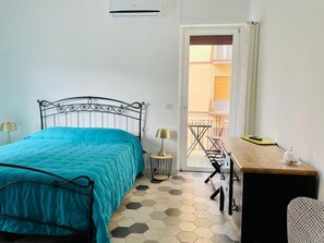 A bedroom with a bed, a desk, a chair, and a view of an outdoor balcony.