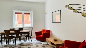 A room with a dining table and chairs, a red armchair, a sofa, a small table with a bowl, and a wall-mounted light fixture. - chiesa russa (Bari)