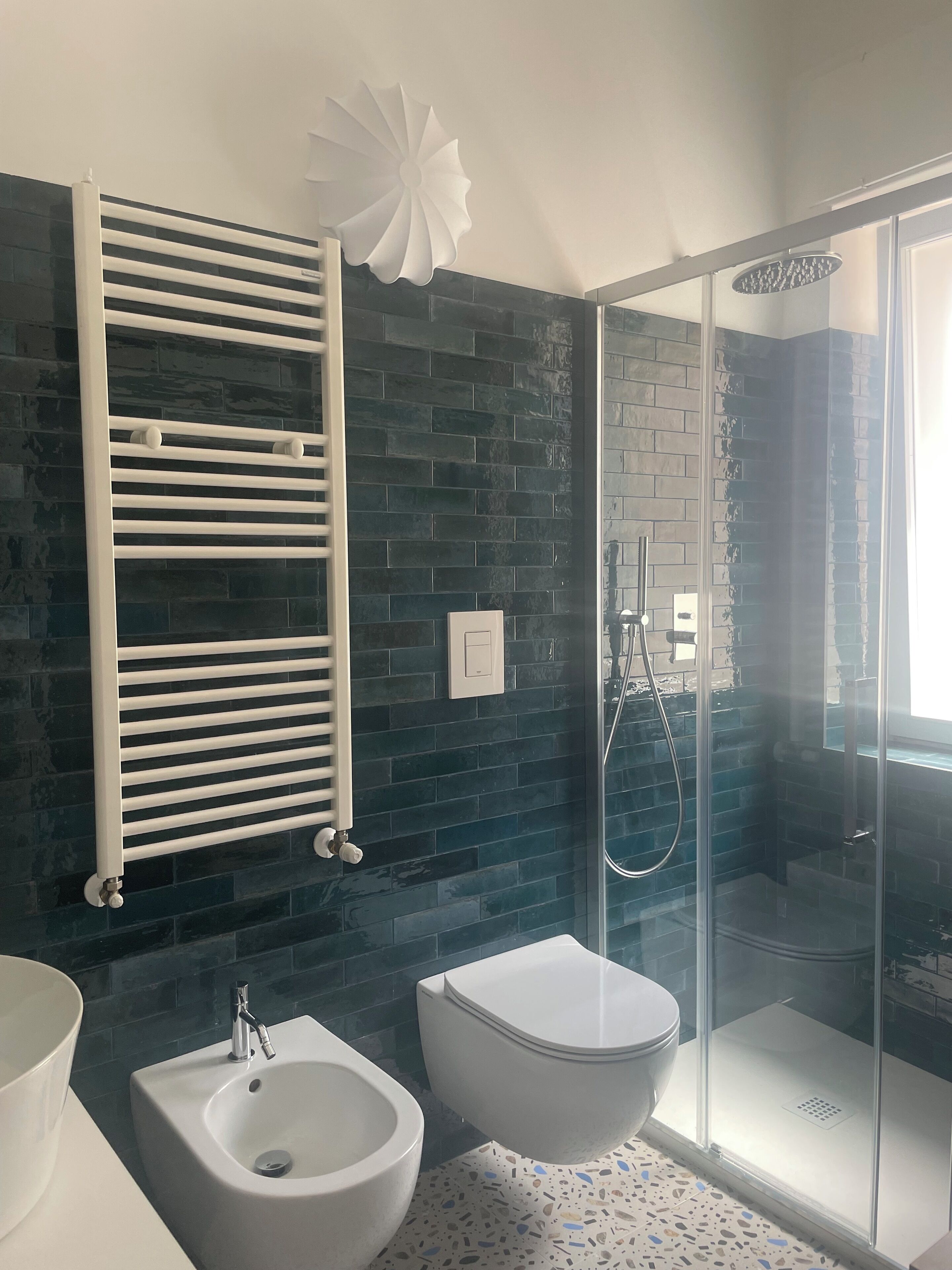 A modern bathroom with a white bathtub, a bidet, a glass-enclosed shower, and a black-tiled wall.