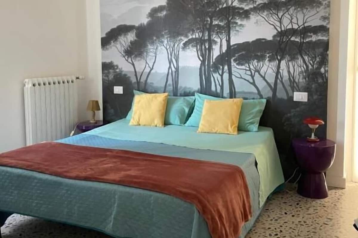 Un dormitorio con cama, radiador, pared con un cuadro y suelo de estampado moteado.