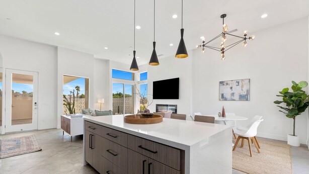 Une cuisine moderne dotée d’un grand îlot central, de luminaires suspendus et d’un coin repas avec une table et des chaises.