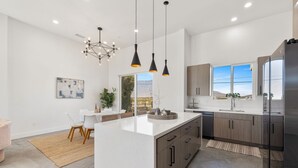 Une cuisine moderne dotée d’un grand îlot central, de luminaires suspendus et offrant une vue sur les montagnes.
