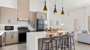 Une cuisine moderne dotée d’un îlot central, de tabourets de bar et de luminaires suspendus.