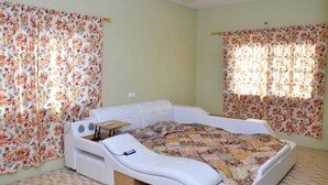 A single-bed room with floral curtains, a small bedside table, and a chair.