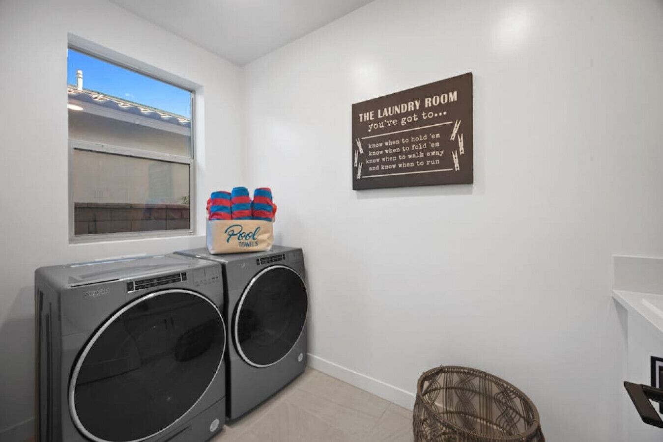 A laundry room with two front-loading washing machines, a basket of pool towels, and a sign on the wall.