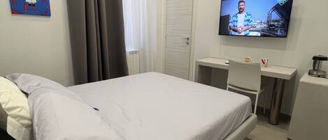 A hotel room with a bed, a desk, a television, and a radiator.