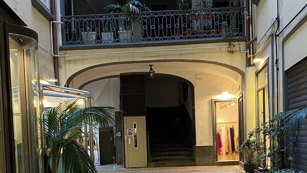Un patio interior con suelo de adoquines, un arco central y una escalera que lleva a un nivel superior.
