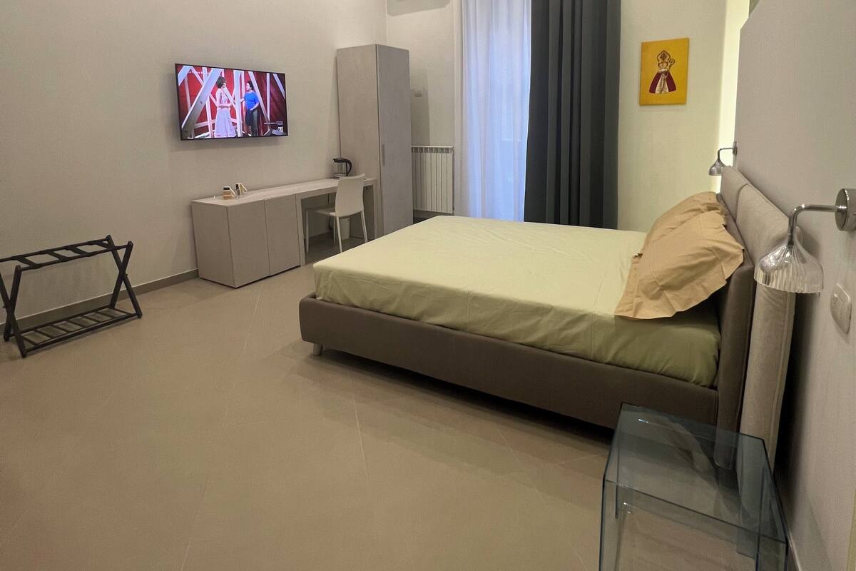 A modern hotel room with a bed, a desk, a chair, a TV, and a radiator.