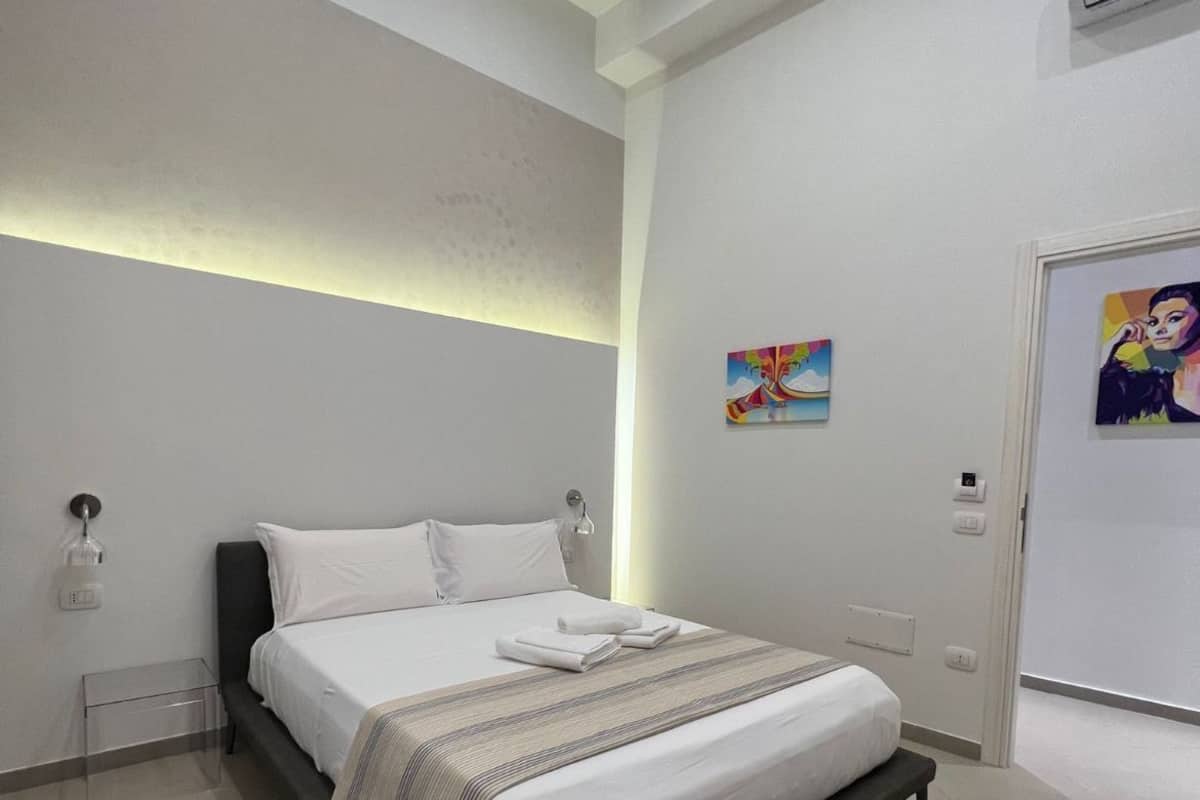 A modern hotel room with a large bed, bedside tables, and a painting on the wall.