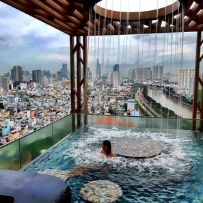 Une personne se détend dans un bain à remous, avec une vue sur un paysage urbain comprenant une rivière et des bâtiments.
