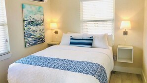 A bedroom with a bed, a painting, two bedside lamps, and a window with blinds. - Wonderful Place w/Private Patio Next to the Beach (Cocoa Beach)
