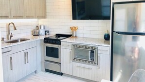 A modern kitchen with light wood cabinets, stainless steel appliances, a built-in microwave, and a flat-screen TV. - Wonderful Place w/Private Patio Next to the Beach (Cocoa Beach)