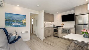 A modern kitchen with white cabinets, stainless steel appliances, and a flat-screen TV. - Wonderful Place w/Private Patio Next to the Beach (Cocoa Beach)