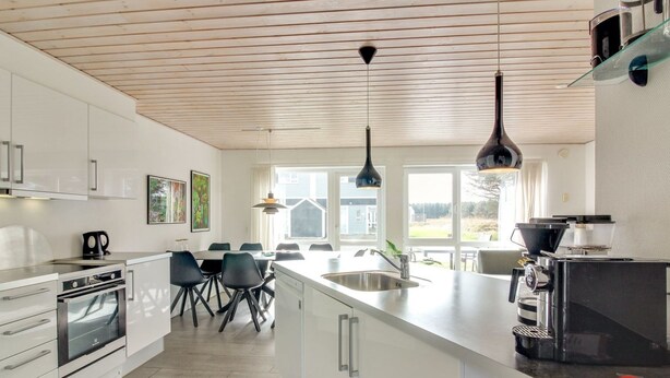 A modern kitchen with white cabinetry, a large island, and a dining area with chairs.