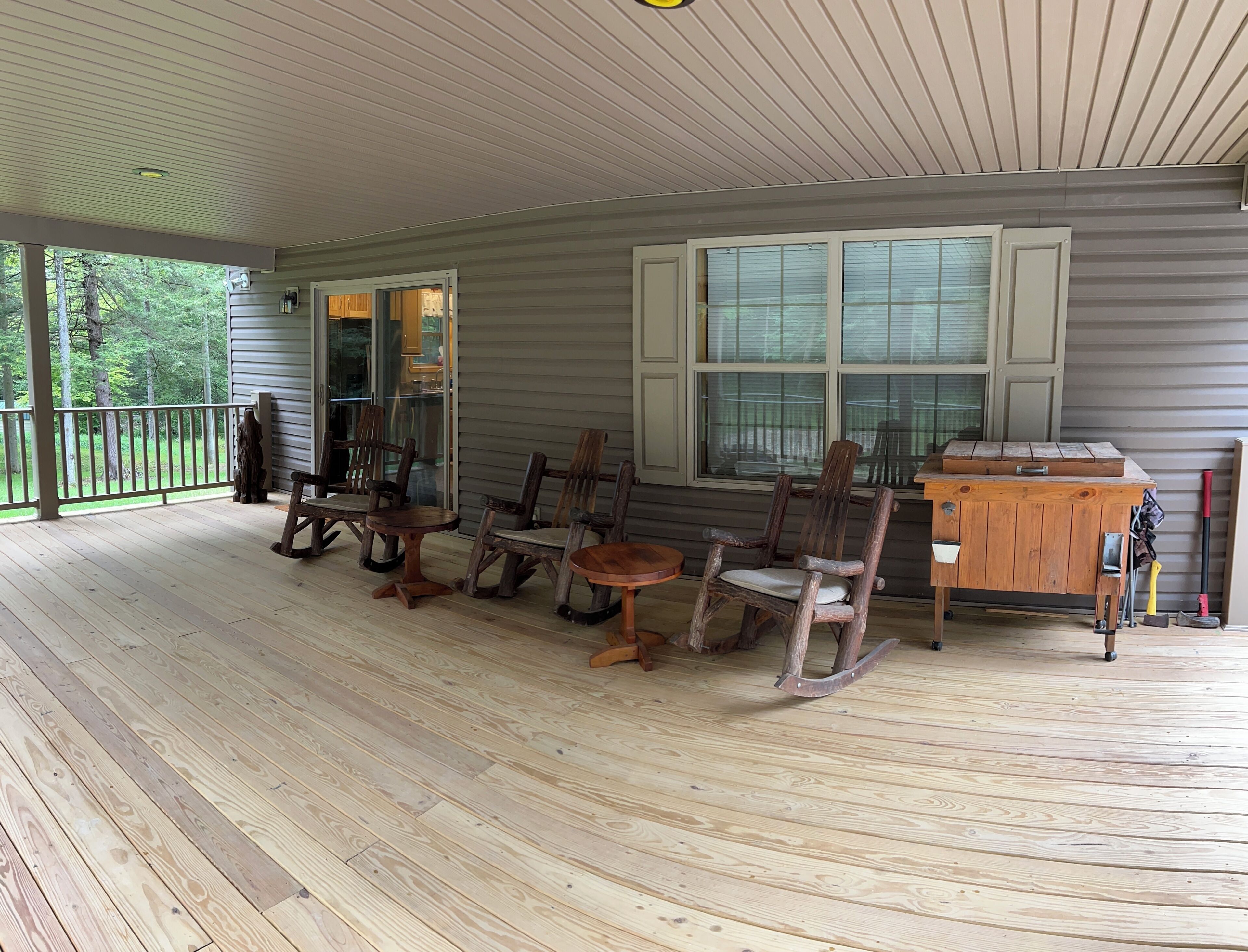 A covered porch with wooden flooring, a dining table with chairs, and a workbench.