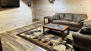 Un salón con pared de madera, un sofá de cuero, una mesa de centro y un televisor montado en la pared.