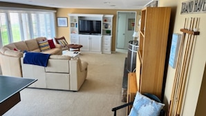 A living room with a beige sofa, a coffee table, and a TV. There is a bookshelf and a door in the background. - Superbly located beachfront house in Grand Haven! Just minutes from Downtown (Spring Lake)