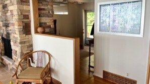 A room with a stone fireplace, a wooden chair, a framed artwork, and a view through a doorway. - Superbly located beachfront house in Grand Haven! Just minutes from Downtown (Spring Lake)
