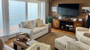 A living room with a sofa, ottoman, and a television on a wooden cabinet. - Superbly located beachfront house in Grand Haven! Just minutes from Downtown (Spring Lake)