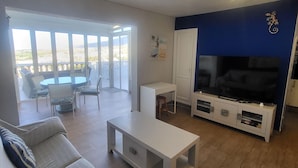 Uma sala de estar com sofá, mesa de centro, rack para TV e varanda com área de refeições.