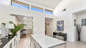 Une cuisine moderne avec des meubles blancs, un îlot central et un coin repas comprenant une table et des chaises blanches.