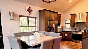 Una cocina moderna con armarios de madera oscura, electrodomésticos de acero inoxidable y un comedor con mesa de vidrio y sillas acolchadas.