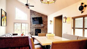 Un comedor con chimenea de piedra, un televisor de pantalla plana encima y una araña.