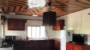 A kitchen with wooden cabinets, a refrigerator, a stove, and a television. - Deux-Palmes-Kribi, close to the beach (200m), comfortable and family-friendly (Kribi)