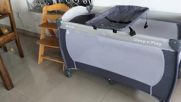 Un berceau portable portant la mention « Sleep n Play », une chaise en bois et un sol carrelé.
