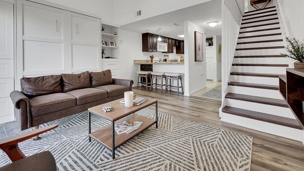 A modern living room with a brown leather sofa, a wooden coffee table, and a patterned rug.
